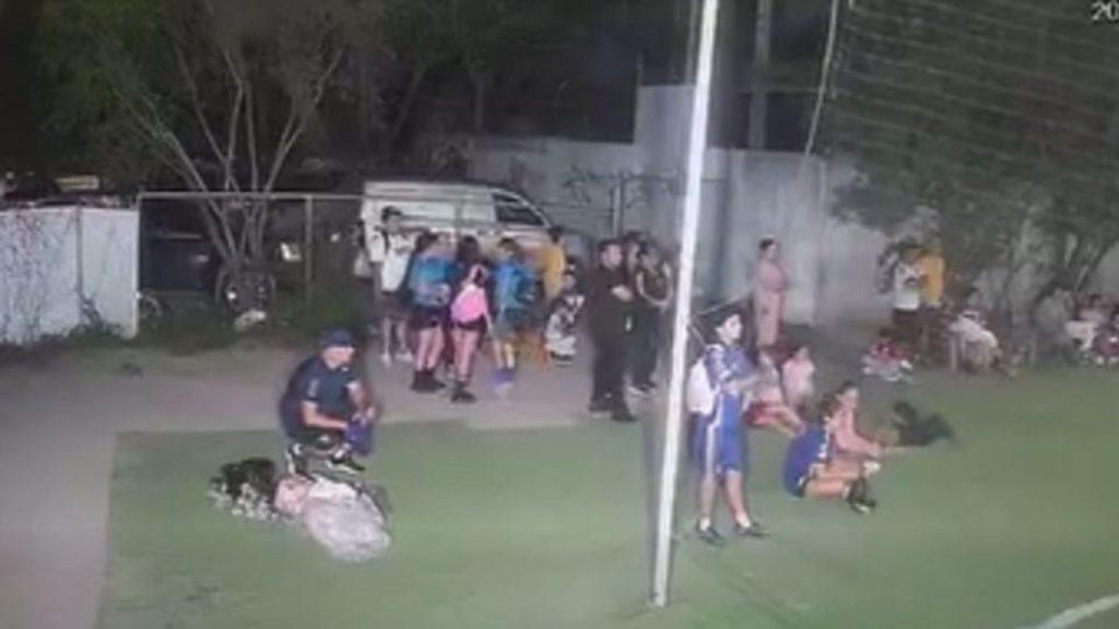 Group of People Standing and Sitting on Grass Near a Tall Flagpole in a Park Setting. | Nl Urbano