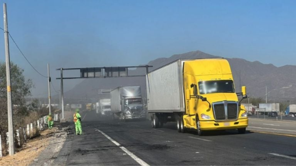 Yellow Semi-truck Driving on a Highway As Road Workers in Green Safety Gear Lay Fresh Asphalt with Mountains in the Distance. | Nl Urbano