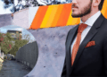 Pintan-barda-naranja-para-ocultar-tejabanes 1 1 | Nl Urbano Man in a Black Suit and Orange Tie Stands Beside a Bright, Striped Mural; a Circular Inset Shows a Narrow, Graffiti-free Alley with Concrete Walls and Greenery Nearby. | Nl Urbano