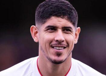 Young Man with Short Dark Hair and a Light Goatee Smiles at the Camera, Wearing a White Jersey with Red Trim. | Nl Urbano