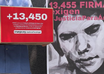 Person in a Blue Shirt Holding a Red Petition Box Labeled '+13,450' Beside a Grayscale Portrait Poster. | Nl Urbano